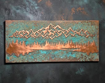 May include: A rectangular metal wall art piece featuring a copper-colored mountain range and a dense forest silhouette layered over a textured, oxidized background with vibrant teal, green, and brown patina finishes across the entire surface.