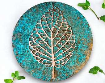 May include: A round, copper-colored wall decor with a turquoise blue background. The decor features a raised, embossed leaf design.