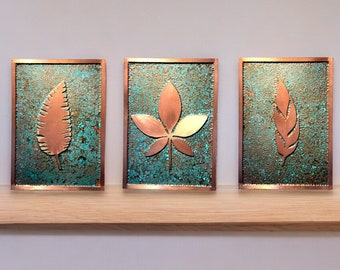 May include: Three copper wall art pieces with a turquoise background. Each piece features a different leaf design.