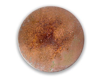May include: A circular metal disc with a weathered copper finish, featuring a mottled texture of deep brown, bronze, and oxidized green patina spots across the surface. The object has a flat, round profile with a distinct metallic sheen.