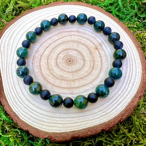 May include: A green and black beaded bracelet with alternating colors. The bracelet is made of round beads and is lying on a wooden surface.