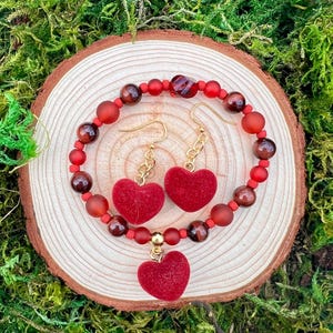 May include: A red heart charm bracelet and earrings set with red and brown beads. The heart charms are made of a soft, fuzzy material.
