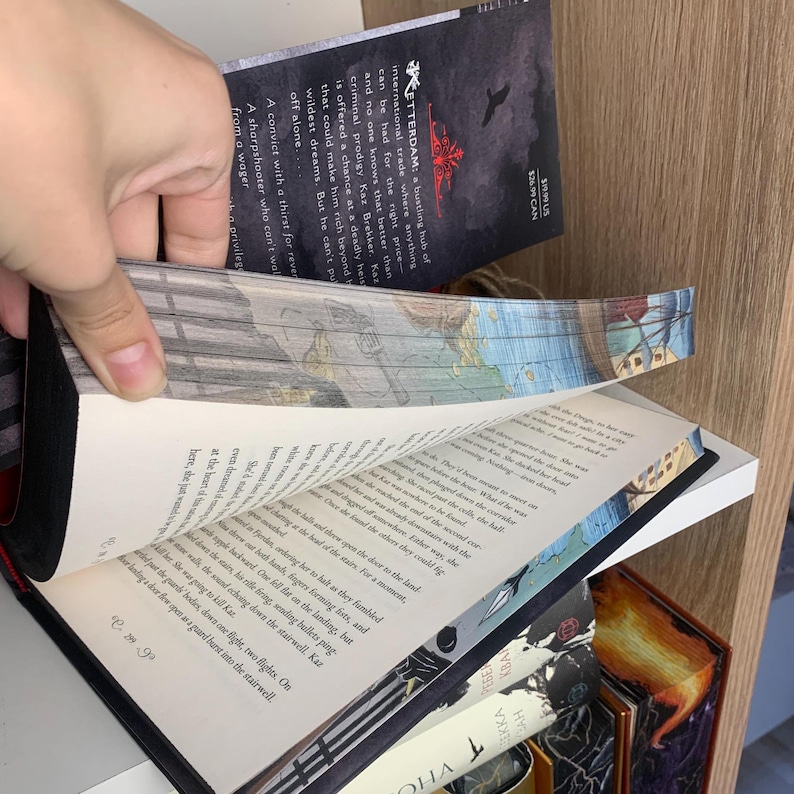Może przedstawiać: Twarda oprawa książki z czarnym grzbietem i przewracanymi stronami. Okładka książki zawiera tekst i ciemną ilustrację. Strony mają wydrukowany tekst. G&oacute;rna część stron ma dekoracyjny wz&oacute;r. Inne książki są widoczne na p&oacute;łce.