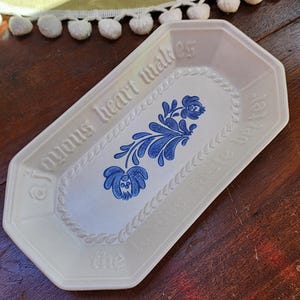May include: A white ceramic rectangular dish with a blue floral design and the text "A joyous heart makes the world a better place".