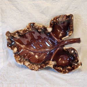 May include: A brown ceramic leaf-shaped serving dish with a brown glaze and a white speckled design. The dish has a raised stem and three sections.