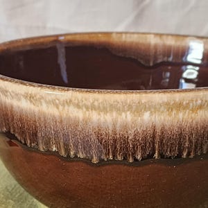 Puede incluir: Un tazón de cerámica marrón con un esmalte blanco y marrón. El tazón tiene un borde ancho y un fondo redondeado.