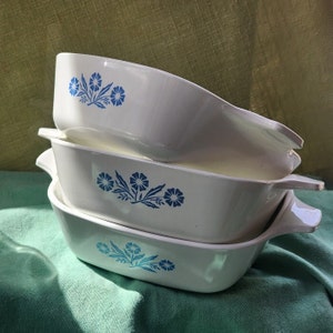 May include: Three white ceramic baking dishes with blue floral designs stacked on top of each other. The dishes are oval shaped with handles on both sides.