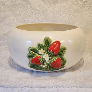 Puede incluir: Un tazón de cerámica blanco con un diseño en relieve de fresas y hojas. Las fresas son rojas con hojas verdes y flores blancas.