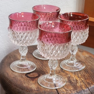 May include: Set of four clear glass stemmed drinking glasses with a ruby red rim. The glasses have a diamond pattern.