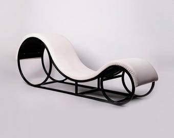 May include: A modern chaise lounge with a curved design. The frame is black, supporting a white cushioned seat. The lounge features a unique, flowing shape, suitable for relaxation. The overall aesthetic is minimalist and contemporary.