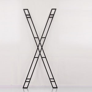 May include: A black metal X-shaped stand with a geometric design. The stand is made of thin metal bars that are welded together to form a criss-cross pattern.