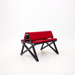 Könnte beinhalten: Eine rote gepolsterte Bank mit einem schwarzen sternförmigen Gestell. Die Bank ist aus Holz und Metall und hat ein modernes Design.