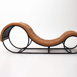 May include: A modern chaise lounge with a brown, tufted seat and a black metal frame. The frame features two large circular supports and a rectangular base. The overall design is sleek and contemporary.