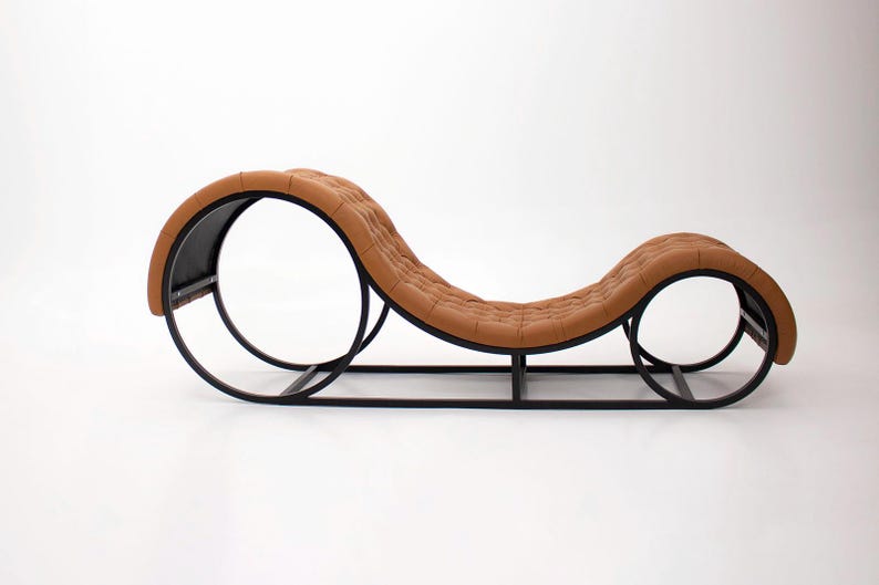 May include: A modern chaise lounge with a brown, tufted seat and a black metal frame. The frame features two large circular supports and a rectangular base. The overall design is sleek and contemporary.