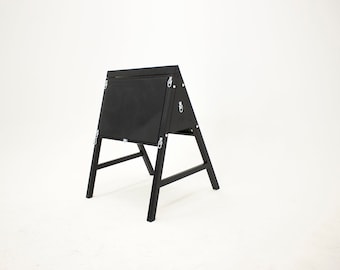 May include: Black wooden A-frame sign with a chalkboard insert. The sign is closed and has two metal clasps on the front.