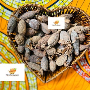 Könnte beinhalten: Ein herzförmiger Korb aus Weidengeflecht, gefüllt mit getrockneten, braunen und faltigen Samen. Der Korb steht auf einem bunten, gemusterten Stoff. Der Text "Afrofoodmart" ist auf einem weißen Etikett sichtbar.