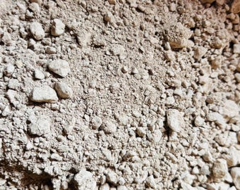 Puede incluir: Primer plano de un montón de pequeñas rocas y grava de color claro. Las rocas varían en tamaño y forma, con una mezcla de texturas lisas y rugosas. El color general es beige apagado, con sutiles variaciones de tono.