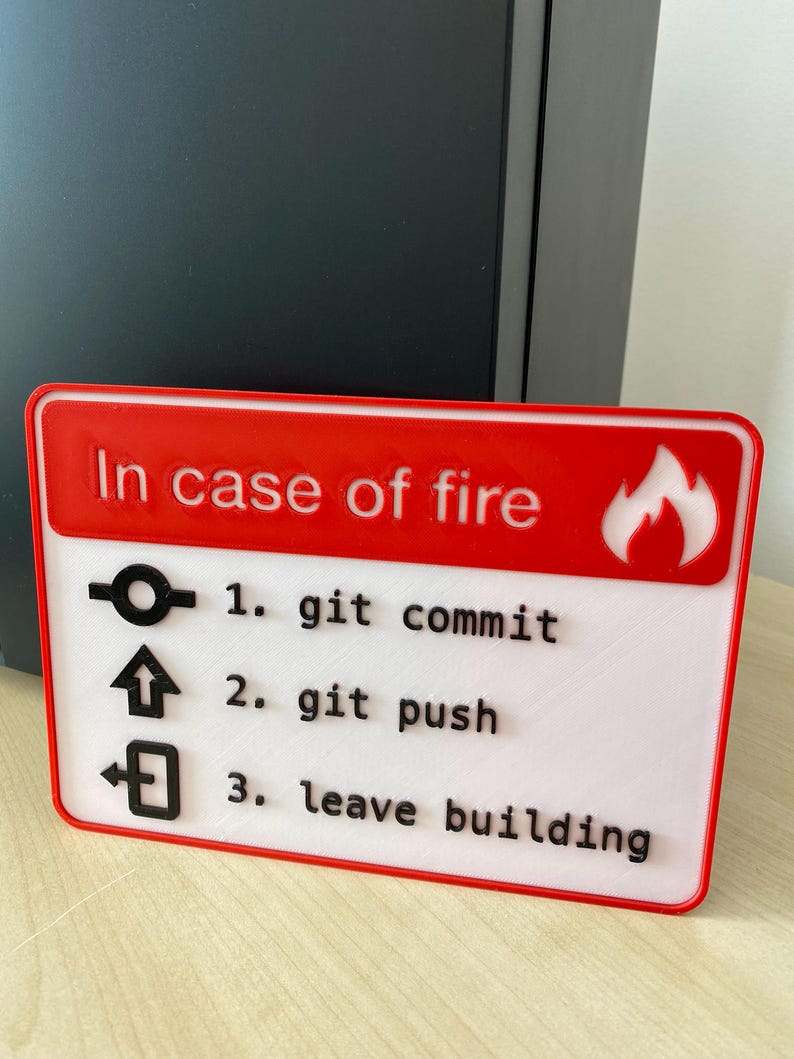 May include: A red and white sign with the text "In case of fire" and a flame icon. The sign lists three steps: 1. git commit, 2. git push, 3. leave building.