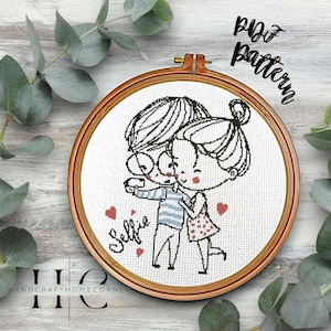 May include: Cross stitch pattern of a couple taking a selfie. The man is wearing a striped shirt and glasses, and the woman is wearing a polka dot dress. The word "selfie" is written below them, and there are hearts around them.