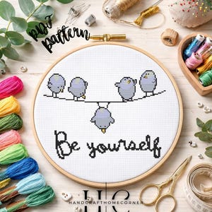 Könnte beinhalten: Ein Kreuzstich-Stickrahmen mit fünf grauen Vögeln auf einer Linie und den gestickten Worten "Be yourself" darunter. Die Worte "PDF pattern" sind kursiv geschrieben. Stickzubehör umgibt den Rahmen.