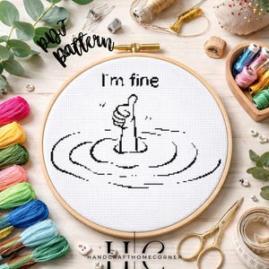 May include: A cross-stitch embroidery hoop with the phrase "I'm fine" and a person's hand giving a thumbs up, surrounded by water ripples. The image includes colorful embroidery floss, scissors, and other craft supplies.