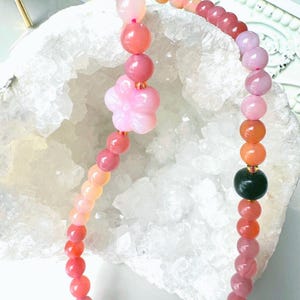 May include: A pink and orange gemstone bracelet with a flower charm. The bracelet is made of round beads and is strung on a clear elastic cord.