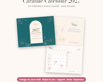 Può includere: Un calendario 2027 Carabae con rilegatura a spirale, copertina color verde ottanio, disegni floreali dorati e un pannello centrale ad arco. Le pagine interne mostrano il mese di maggio con una griglia, note e dettagli color rosa.