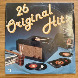 May include: A vintage vinyl record album titled "26 Original Hits" with a retro design. The album cover features a stylized image of a record player, records, and a glass of Coca-Cola. The album is sealed in plastic.
