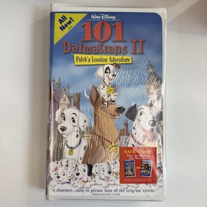 Puede incluir: Una cinta VHS sellada de "101 Dálmatas II: La aventura londinense de Patch" de Disney. La portada presenta dálmatas, el horizonte de Londres y el texto "All New!" y "Save 4 Now".