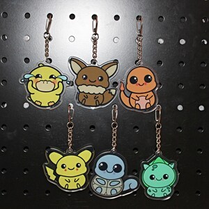 May include: Six acrylic keychains featuring cartoon characters. The keychains include a yellow duck, a brown fox, an orange lizard, a yellow mouse, a blue turtle, and a green plant-like creature. Each keychain has a silver chain and clasp.