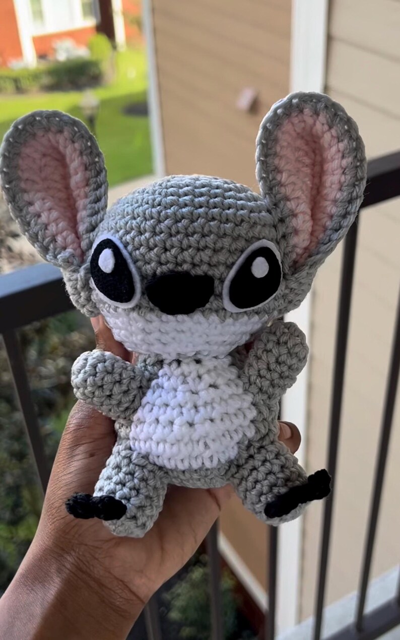 Puede incluir: Un juguete de peluche gris tejido a crochet con grandes ojos negros y una barriga blanca. El juguete tiene orejas grandes y una nariz negra cosida.