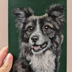 Puede incluir: Retrato pintado de un perro con pelaje negro, gris y blanco, sobre un fondo verde oscuro. El perro tiene ojos marrones y una expresión feliz. La obra de arte está sobre un pequeño lienzo.