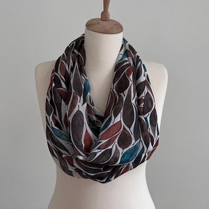 Peut inclure: Une écharpe infinie blanche, marron et turquoise avec un motif de feuilles.
