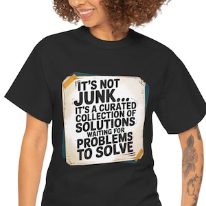 Peut inclure: T-shirt noir avec l'inscription "IT'S NOT JUNK... IT'S A CURATED COLLECTION OF SOLUTIONS WAITING FOR PROBLEMS TO SOLVE" dans un design rectangulaire. Le t-shirt est porté par une personne.