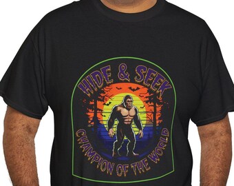 Könnte beinhalten: Schwarzes T-Shirt mit einer grünen, violetten und orangenen Grafik eines Bigfoot-Charakters in einer Waldlandschaft. Die Grafik lautet "Hide & Seek Champion of the World".