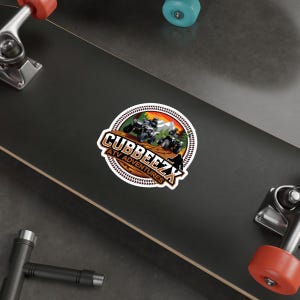 Può includere: Un adesivo marrone e arancione con il testo "Cubbeezx ATV Adventures" e una grafica di tre ATV che guidano attraverso una foresta.