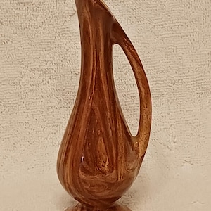 Könnte beinhalten: Eine braune Keramikvase mit einer einzigartigen, länglichen Form und einem Henkel. Die Vase hat eine glänzende Oberfläche und ein marmoriertes Muster in Braun- und Beigetönen. Die Vase ist etwa 20 cm hoch.
