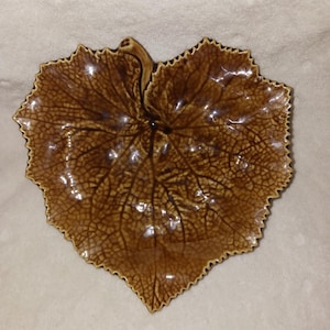 May include: A brown, leaf-shaped ceramic dish with a textured surface and detailed vein patterns. The dish has a scalloped edge and a glossy finish, resembling a natural leaf. Ideal for serving snacks or as a decorative piece.