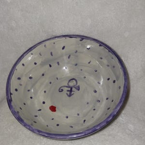 May include: Hand-painted ceramic bowl with a white interior, adorned with small purple dots and a purple rim. Features a purple symbol and a small red dot. A decorative and functional piece.