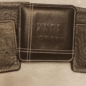 Könnte beinhalten: Eine weiße Keramik-Tasse mit schwarzem Henkel und dem Text "But First, Coffee" in schwarzer, handschriftlicher Schrift. Die Tasse steht auf einer weißen Oberfläche.