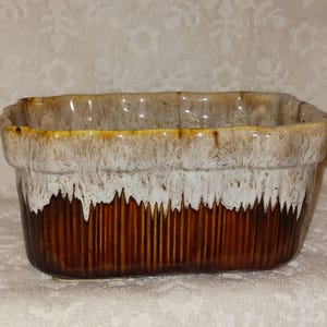 May include: Rectangular ceramic baking dish with a brown, white, and tan glaze. The dish has vertical ridges on the sides and a dripped glaze effect. The interior is a light tan colour.