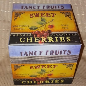 Puede incluir: Una caja decorativa con un diseño vintage. La caja presenta las palabras "Fancy Fruits", "Sweet" y "Cherries". La caja tiene un fondo amarillo con una ilustración de cerezas y el texto "Washington's Favorite" y "Since 1776".