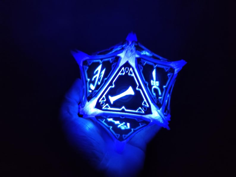 May include: A blue glowing 3D printed D20 dice with a white outline and black numbers. The dice is being held in a hand.