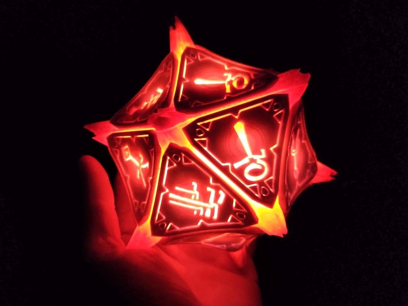 May include: A red glowing 10-sided die with black and white markings. The die is made of a translucent material and is lit from within.