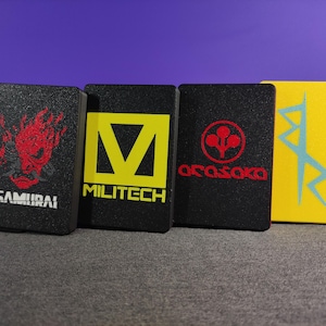 May include: Four rectangular panels with textured surfaces and logos. The first is black with a red samurai face and the word "SAMURAI". The second is black with a yellow "V" and the word "MILITECH". The third is black with a red logo and the word "ARASAKA". The fourth is yellow with a blue design.