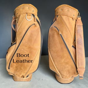 Puede incluir: Dos bolsas de golf de cuero marrón con ribetes y cremalleras negras. Las bolsas tienen un acabado envejecido e incluyen una correa para el hombro y un asa. El texto "Boot Leather" es visible en una de las bolsas.