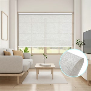 May include: White blackout roller shades with a textured fabric. The shades are installed in a living room with a couch, coffee table, and plants.