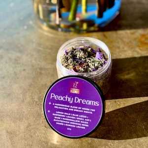 Peut inclure: Un pot en verre rempli d'herbes et de fleurs séchées, étiqueté "Peachy Dreams" avec une liste d'ingrédients comprenant de la mélisse, du lotus bleu, des feuilles de framboise, du casque, de la guimauve, de la calea, du zacatechichi, des roses et des feuilles de damiana. Le pot est posé sur une surface en bois.