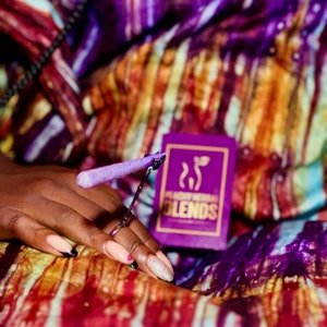 Peut inclure: Une boîte violette et dorée avec le texte "Heady Herb Blends" dessus. Une main tient un outil de roulage violet et argenté avec un pré-roulé violet.