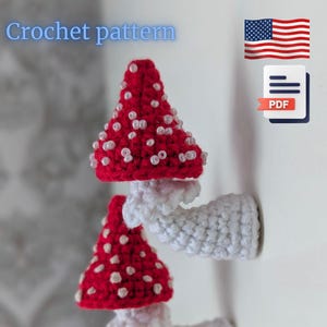 May include: Crochet pattern for mushroom decor. The image shows two handmade crochet mushrooms with red caps and white spots, adorned with small white beads. The stems are white. The text "Crochet pattern" is visible.